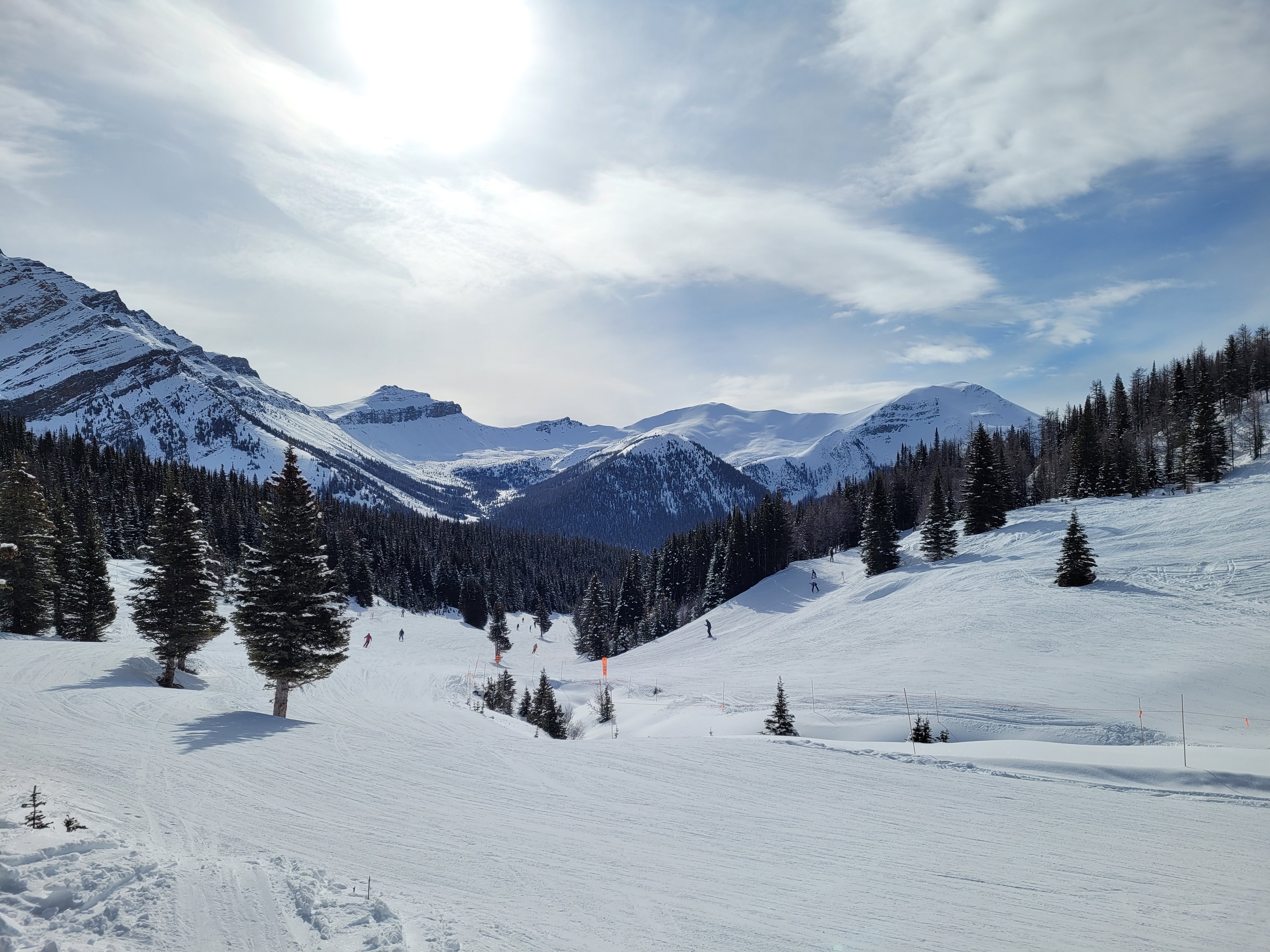 Snow-covered ski slopes at Lake Louise with skiers and mountain peaks under a bright blue sky